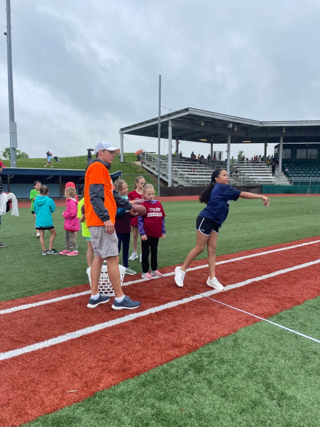 Girl throwing a football at Homeschool Field Day as a coach and other kids watch