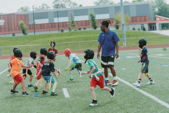 Kids playing flag football with a coach on the turf field